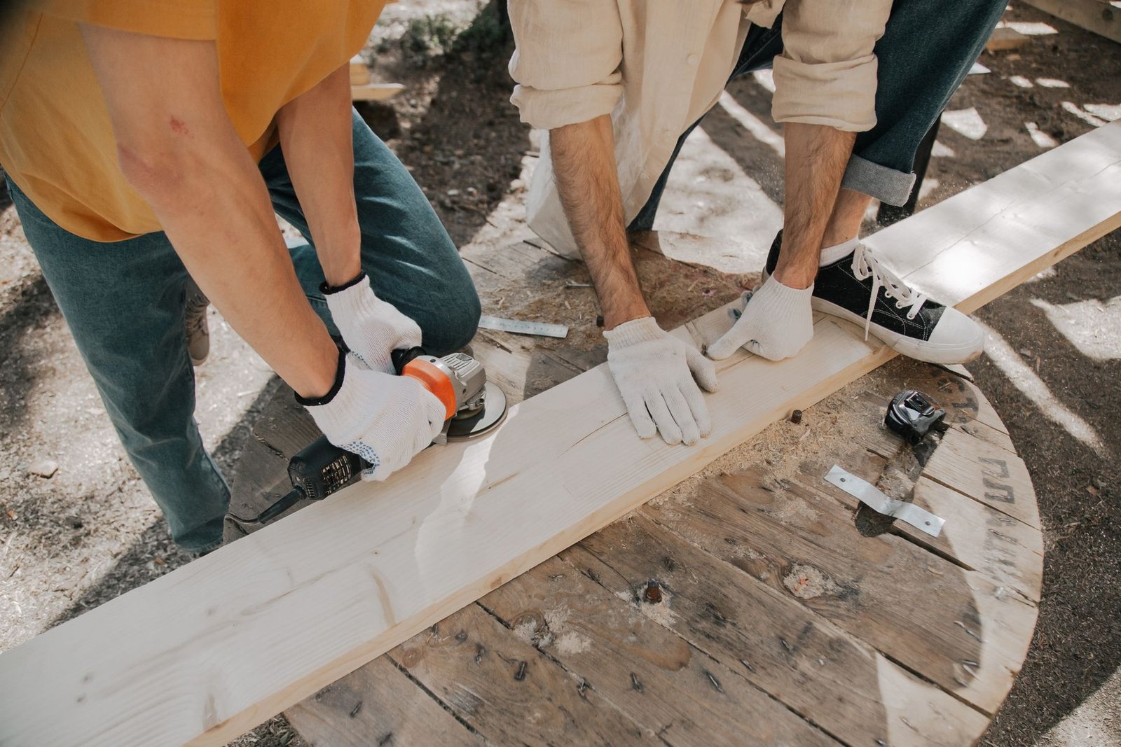 Two carpenters cutting a board with power tools on site