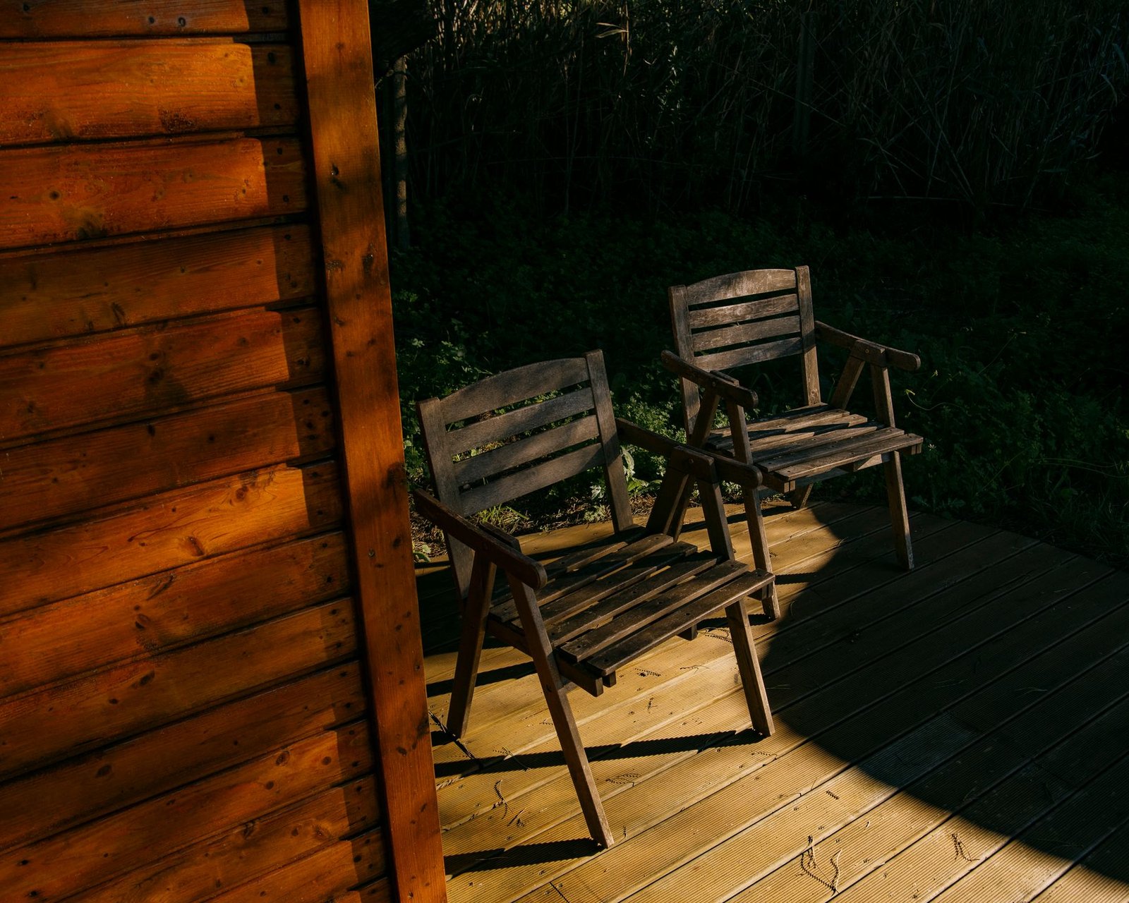 Wooden chairs on a sunlit deck beside a timber cabin