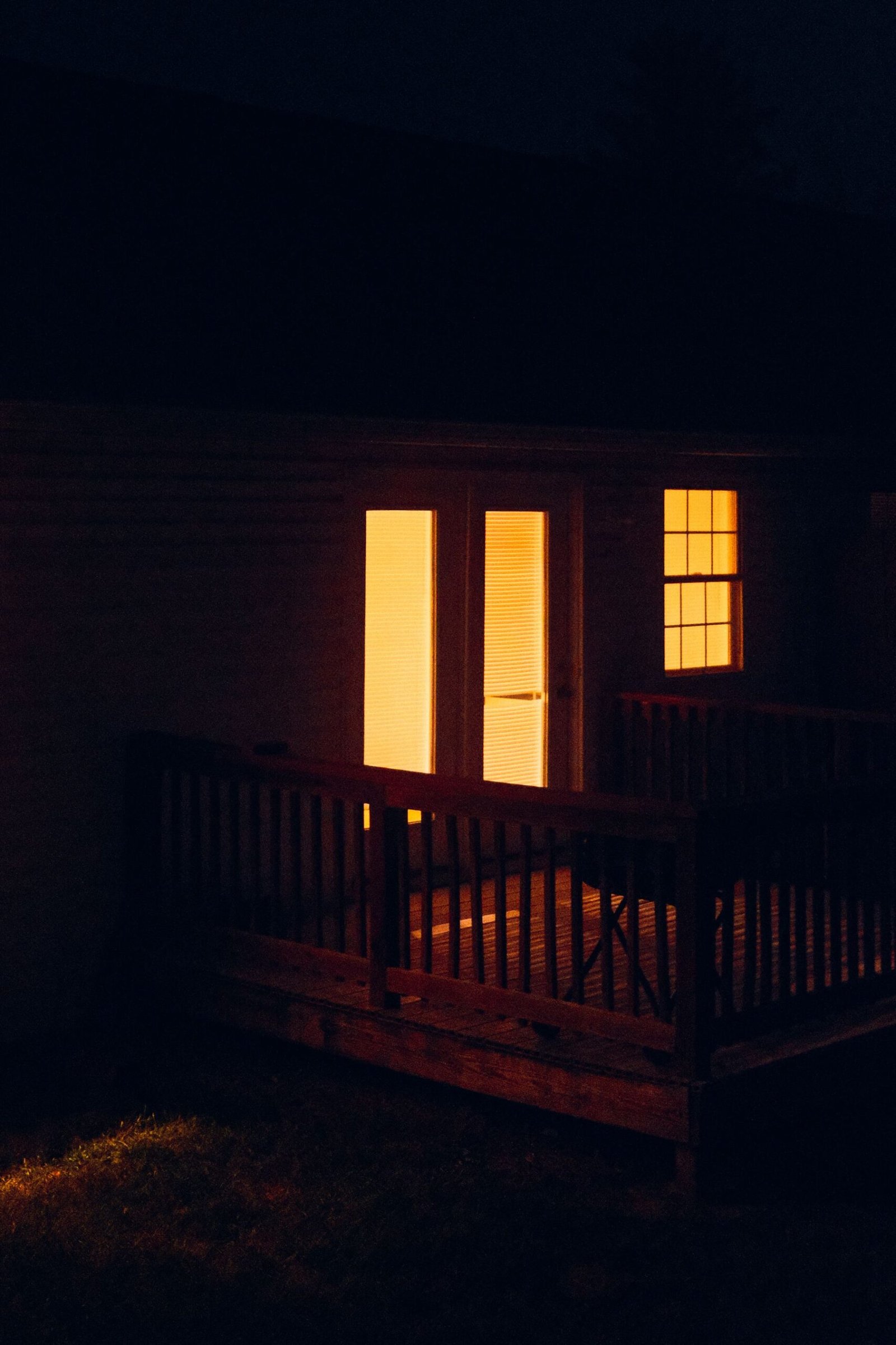 Wood terrace lit at night with warm light from the house windows